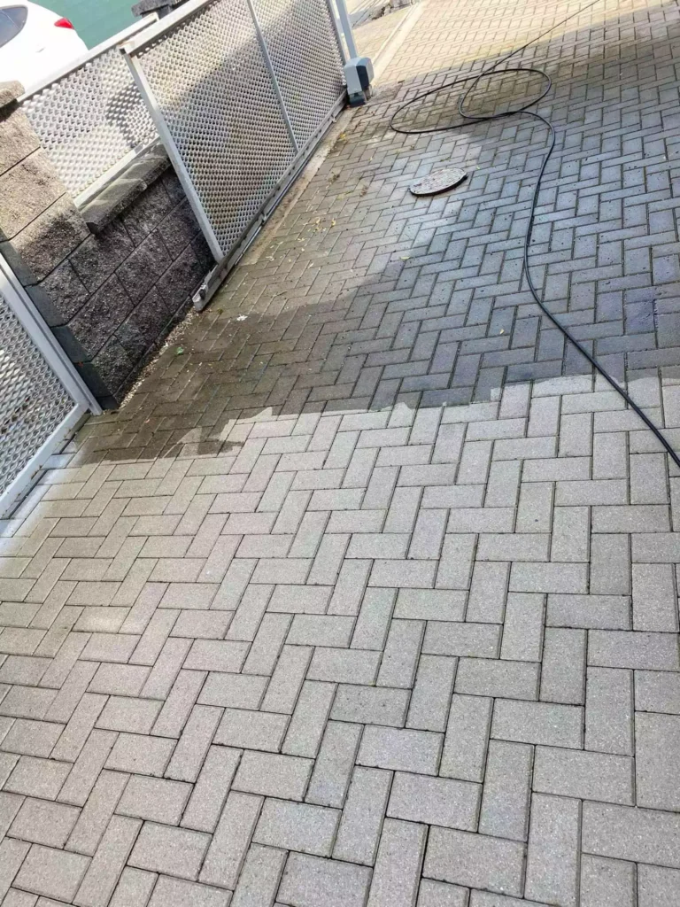 Vysokotlakové čistenie zámkovej dlažby v priebehu realizácie – viditeľná hranica medzi vyčistenou svetlou plochou a znečistenou tmavou časťou pri vstupnej bráne